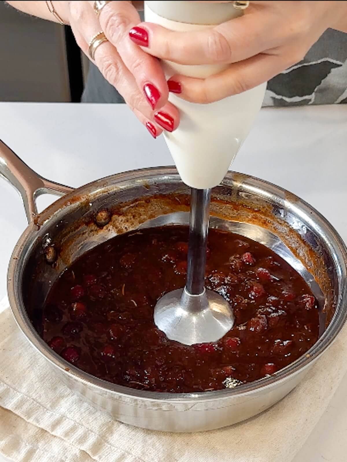 An immersion blender mixing a bowl of cranberry bbq sauce.