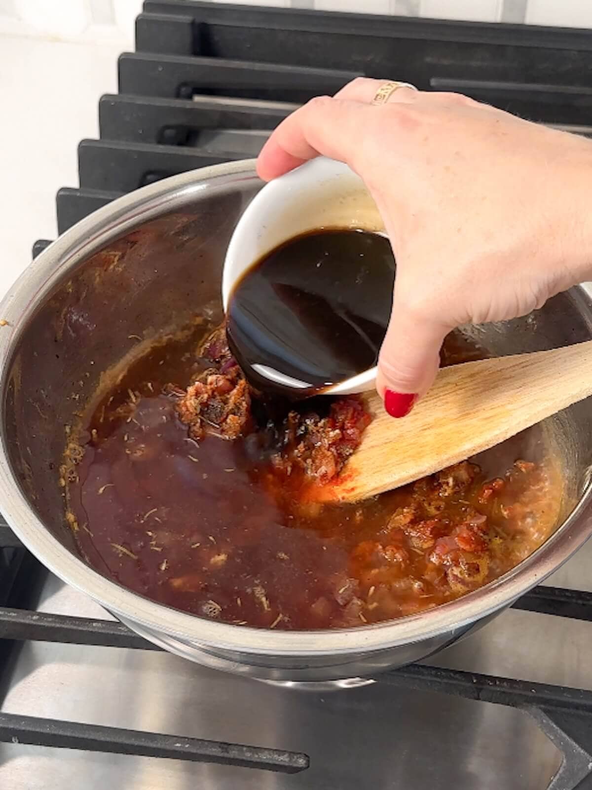 Hand pouring Worcestershire sauce into a bowl of other bbq sauce ingredients.