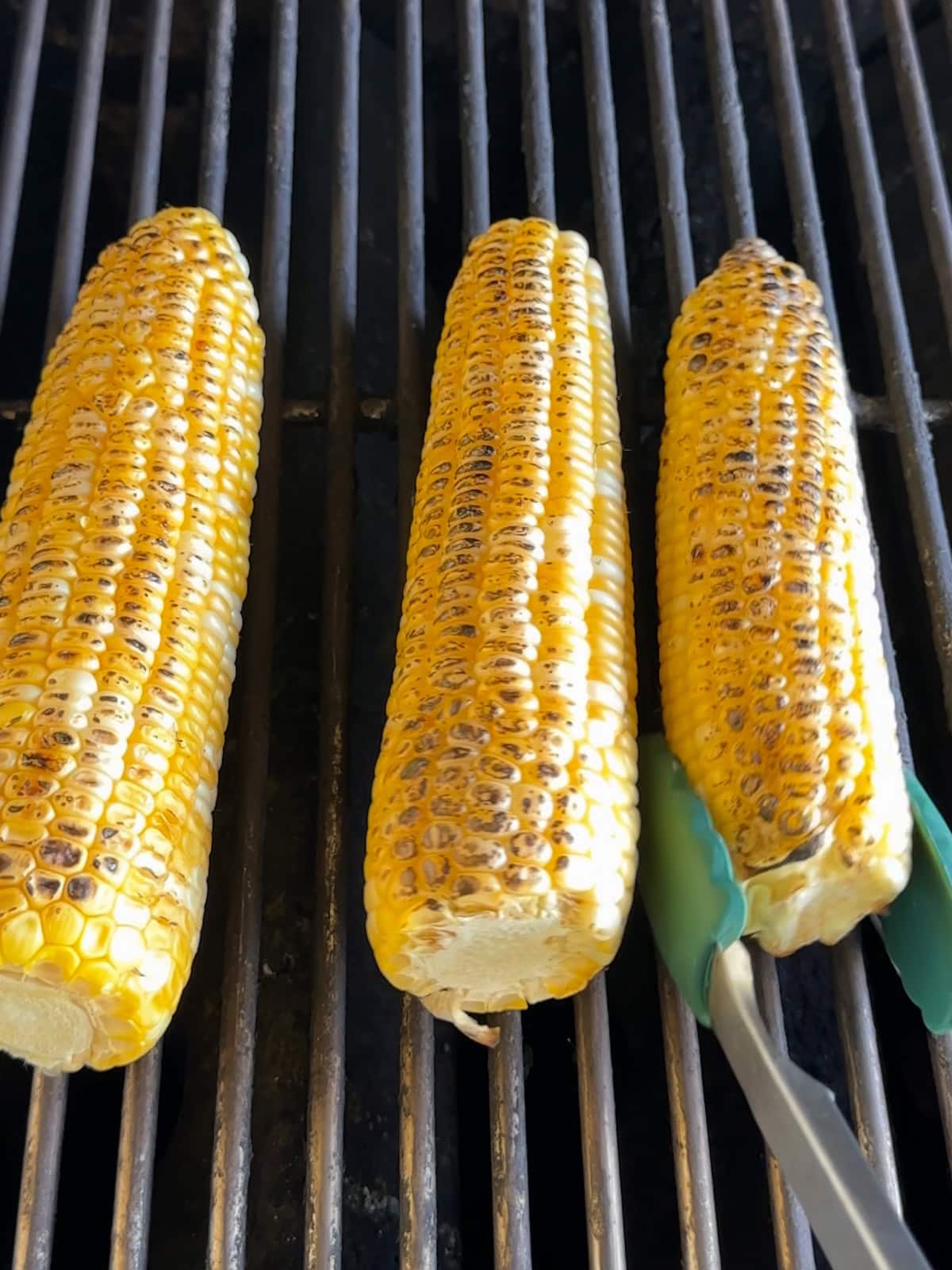Three ears of grilled corn on a grill.