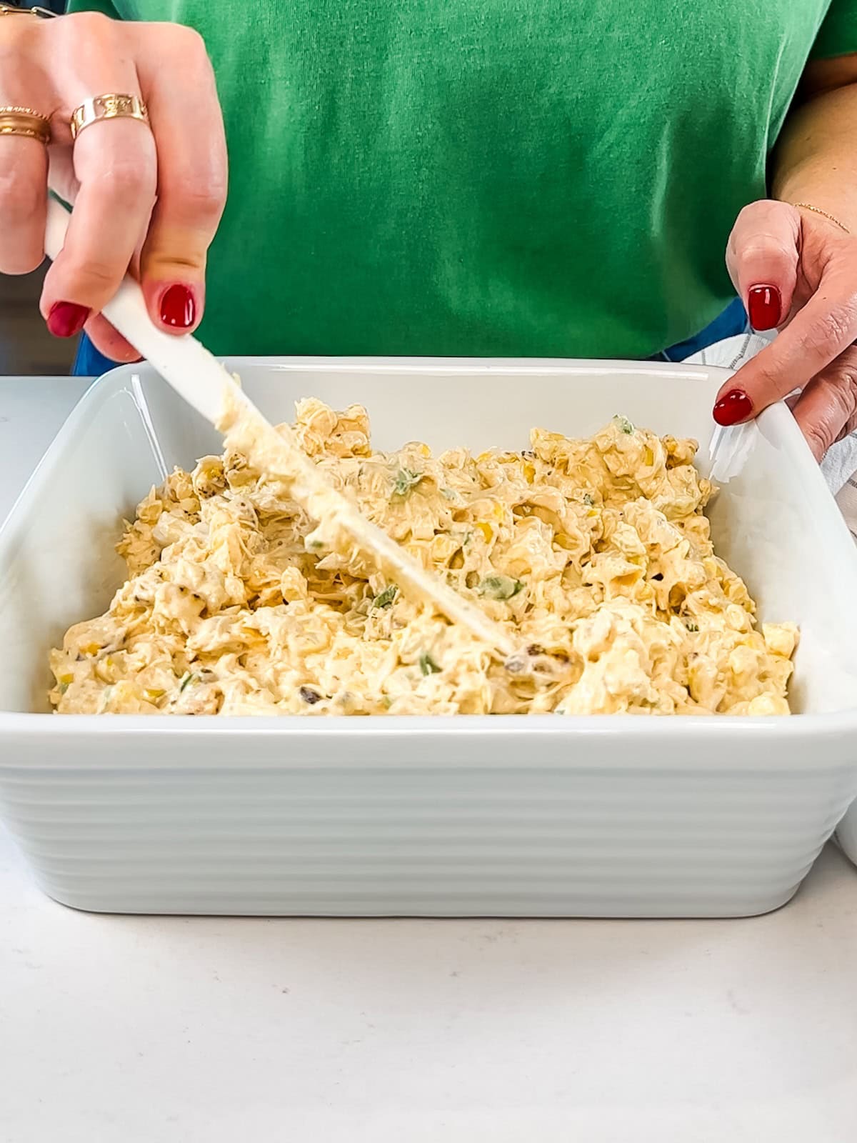 Hand spreading crab dip in a ceramic container.
