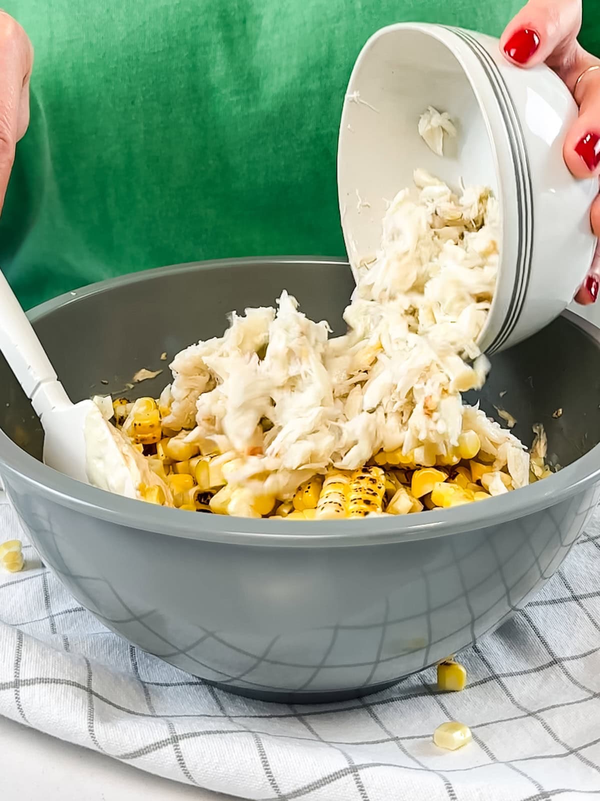 Adding crab meat to a bowl with other crab dip ingredients like grilled corn.