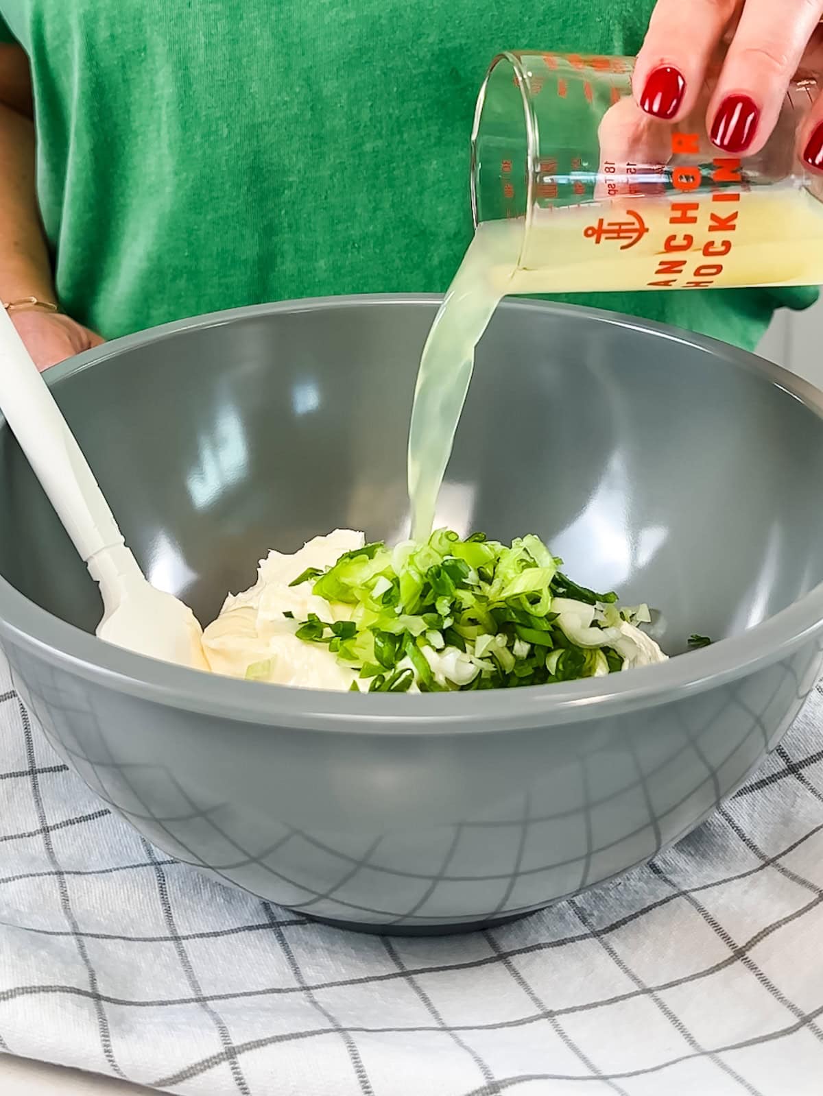 Pouring lemon juice into a bowl with other crab dip ingredients like scallions and mayonnaise.
