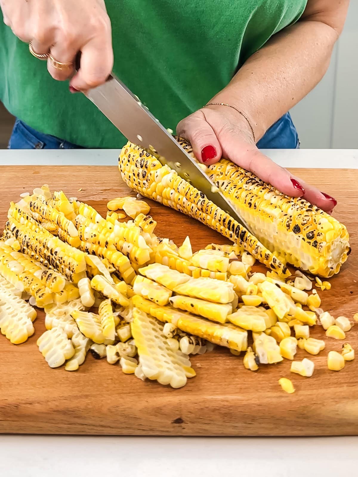 Using a large sharp knife to cut off grilled corn kernels.