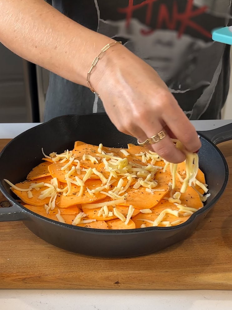 Sprinkling cheese over sliced sweet potatoes.