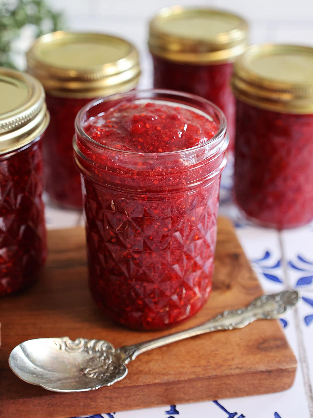 A jar of raspberry freezer jam next to a silver spoon.