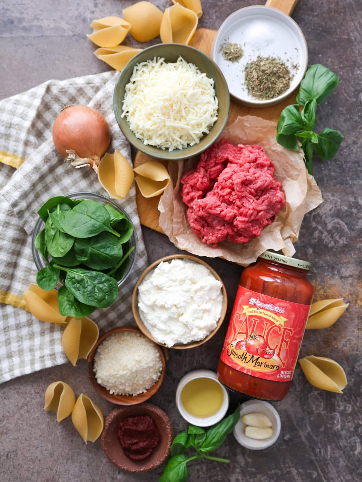 Ingredients needed to make beef and ricotta stuffed shells, including ground beef, ricotta, mozzarella, marinara, spinach, onion and seasonings.