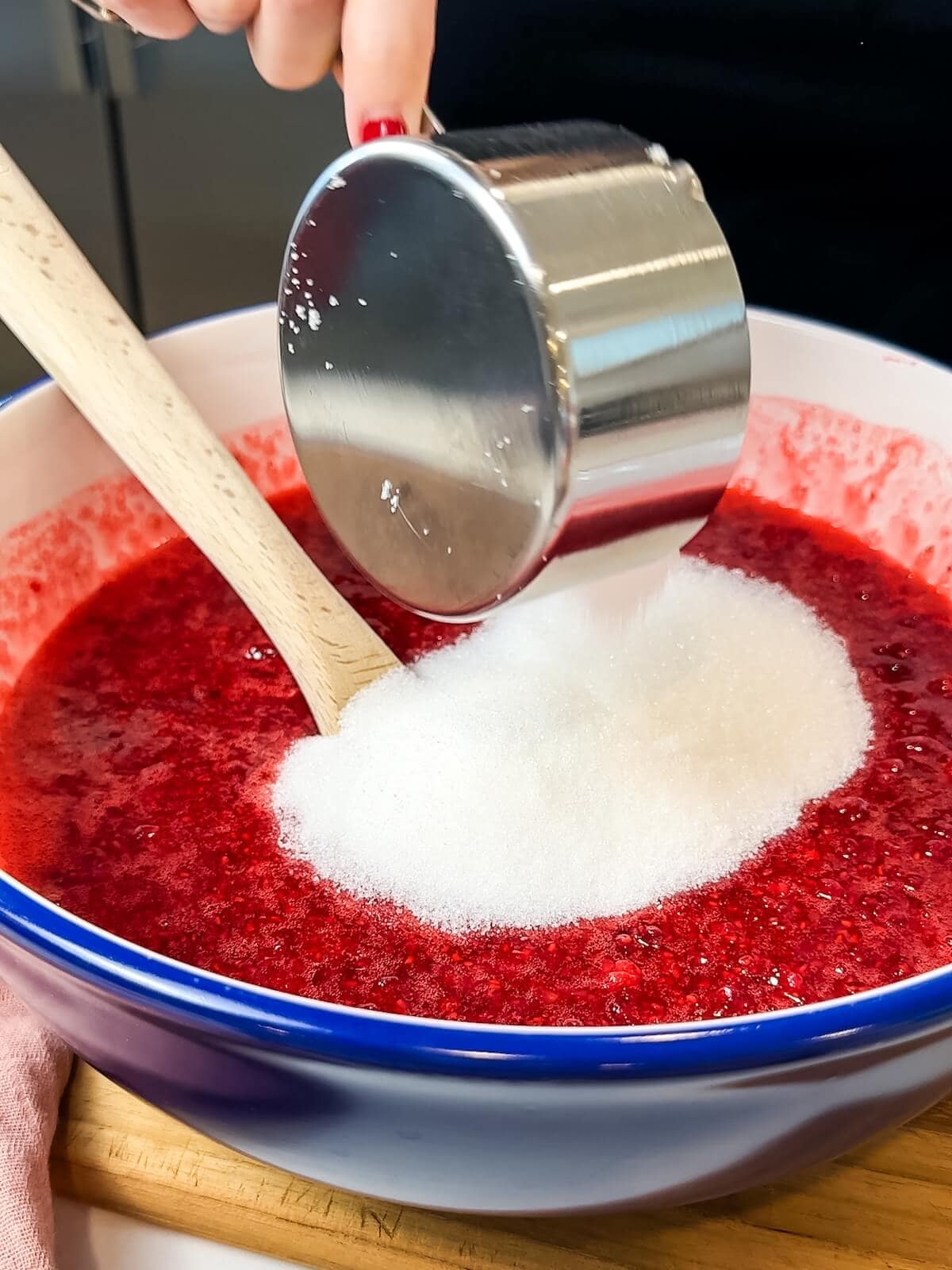 adding sugar to mashed raspberries in a bowl.