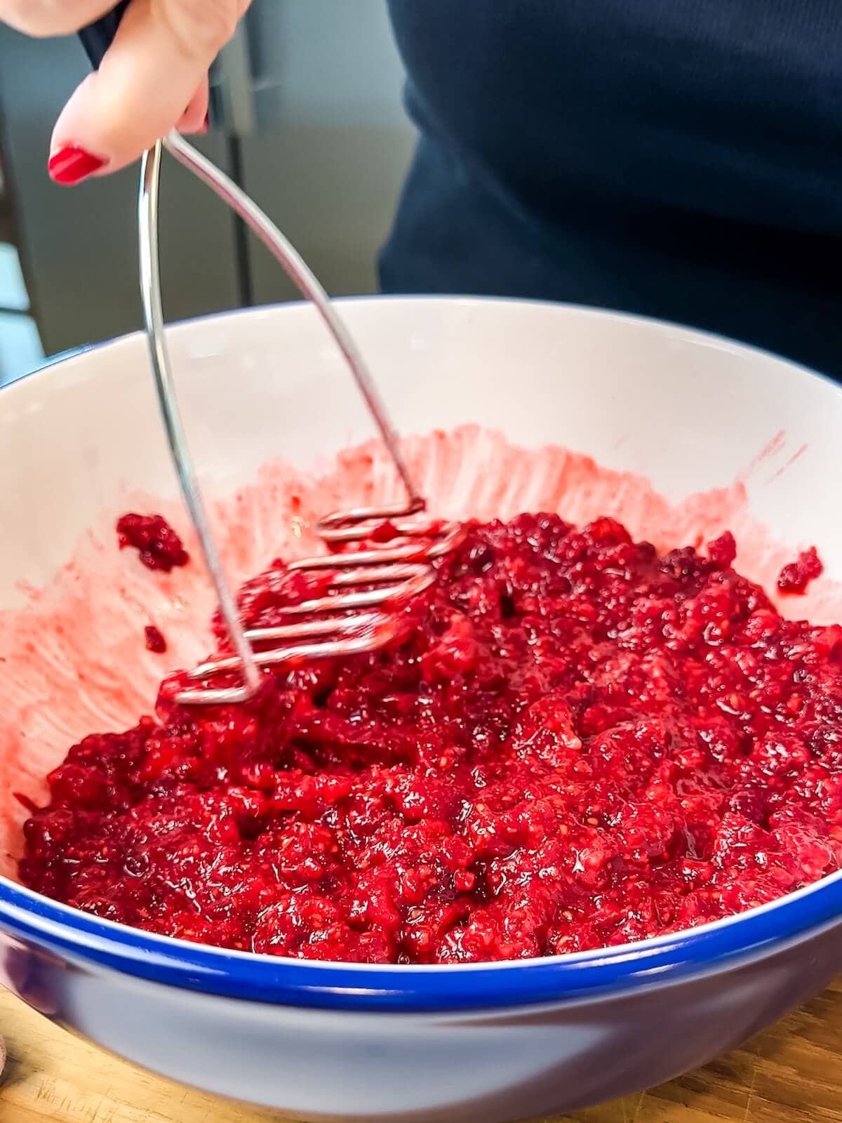 Mashing raspberries with a potato masher.