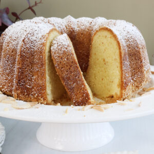 Close up of an almond pound cake on a cake plate with a few slices removed.