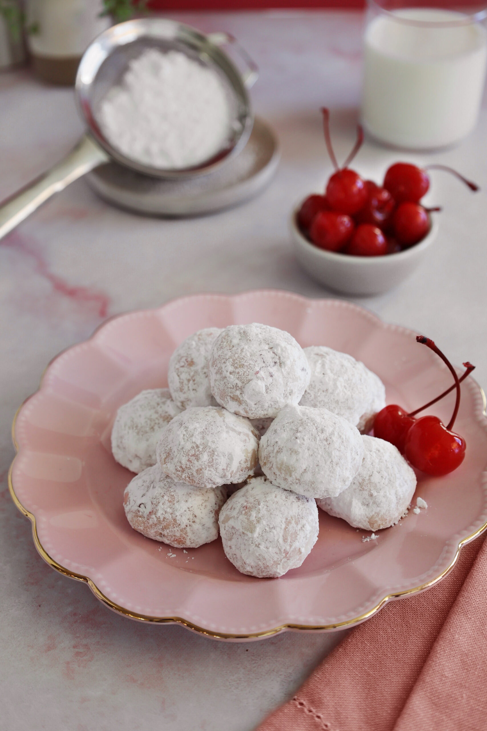 A pink plate piled with cherry almond cookies next to cherries.