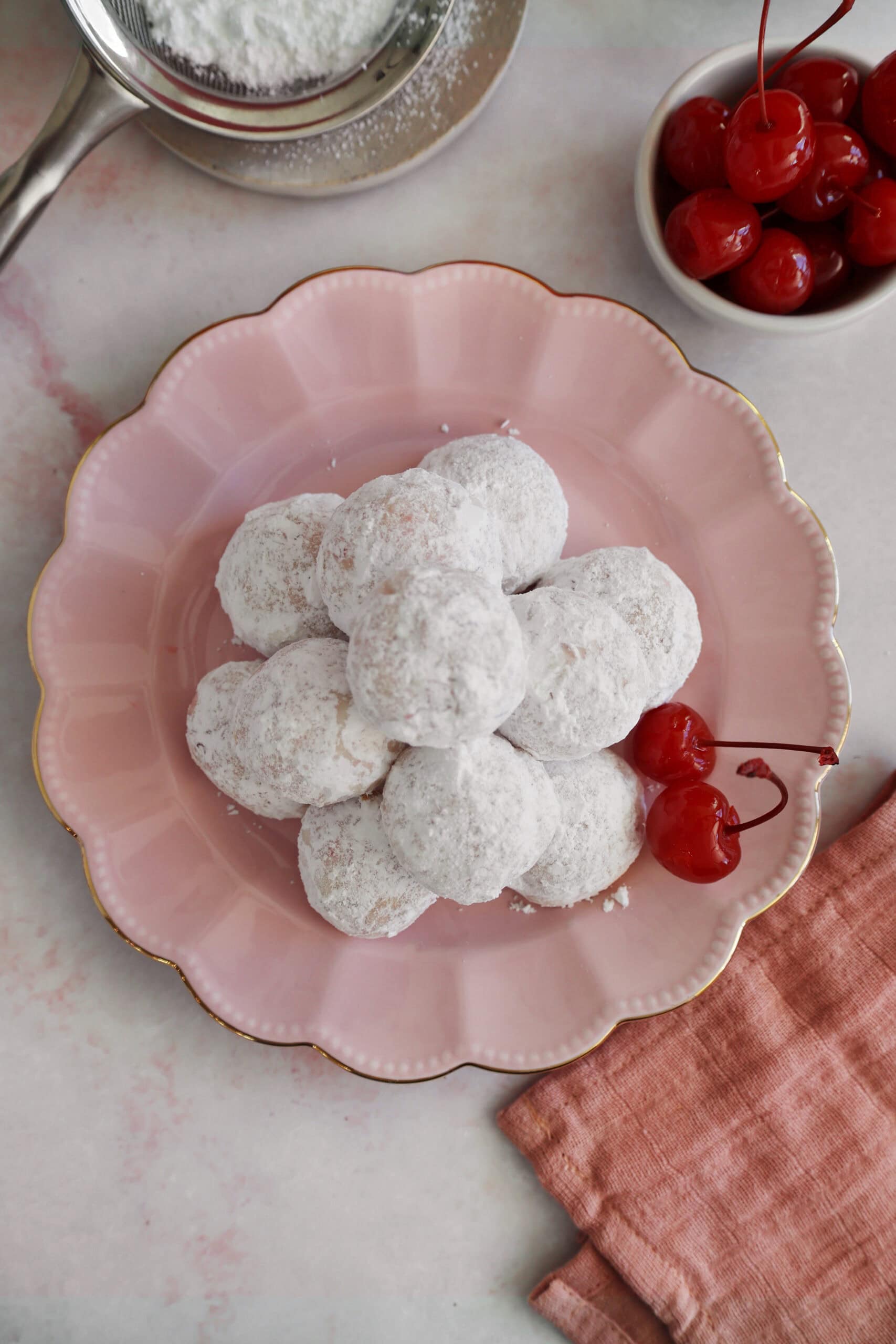 Overhead view of cherry almond cookies piled on a pink plate next to cherries.