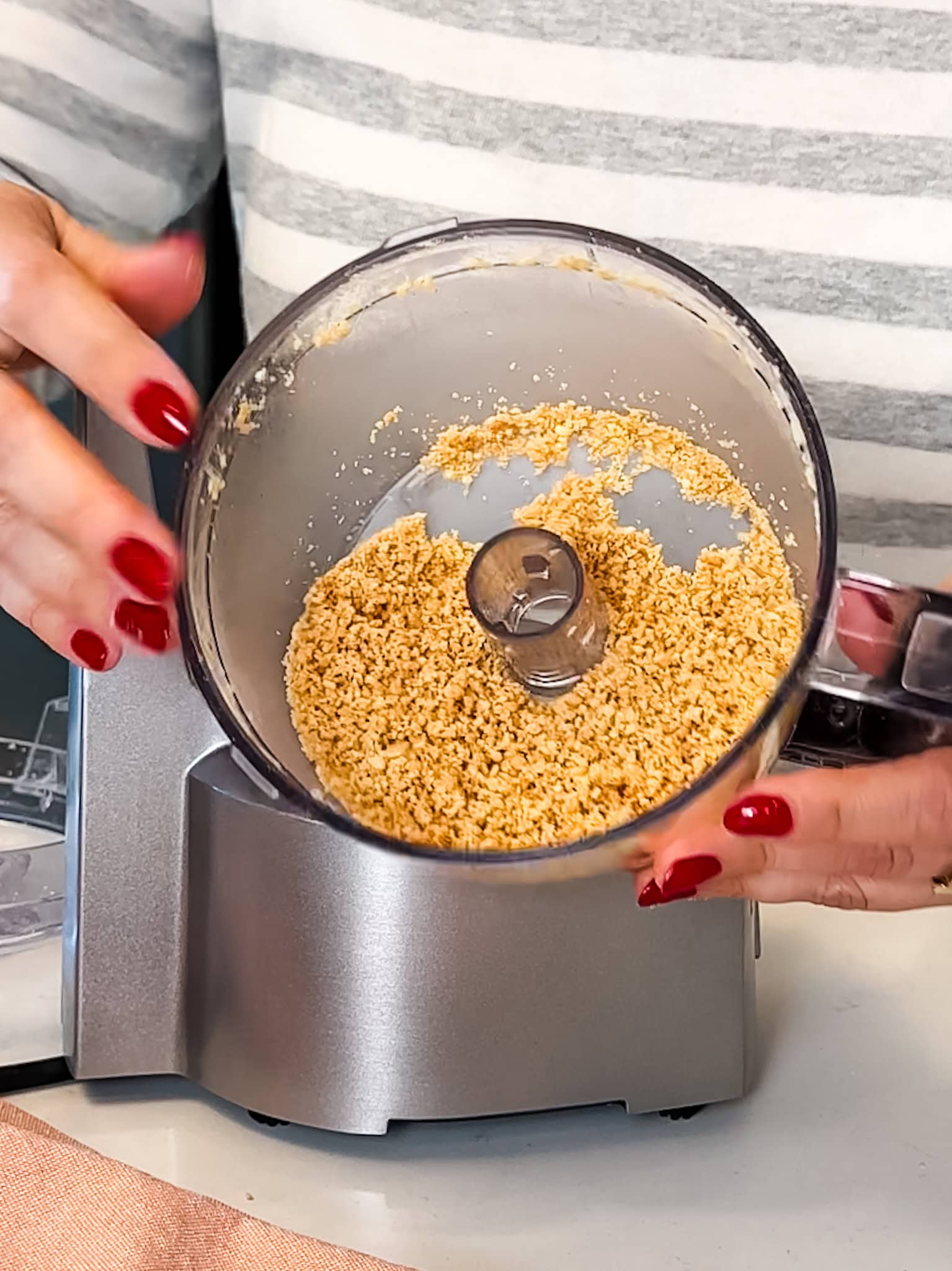 Hands displaying the inside of a food processor filled with ground almonds.