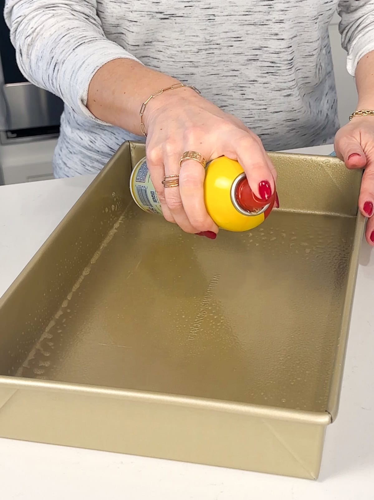 greasing a pan for soft cornbread using oil spray.