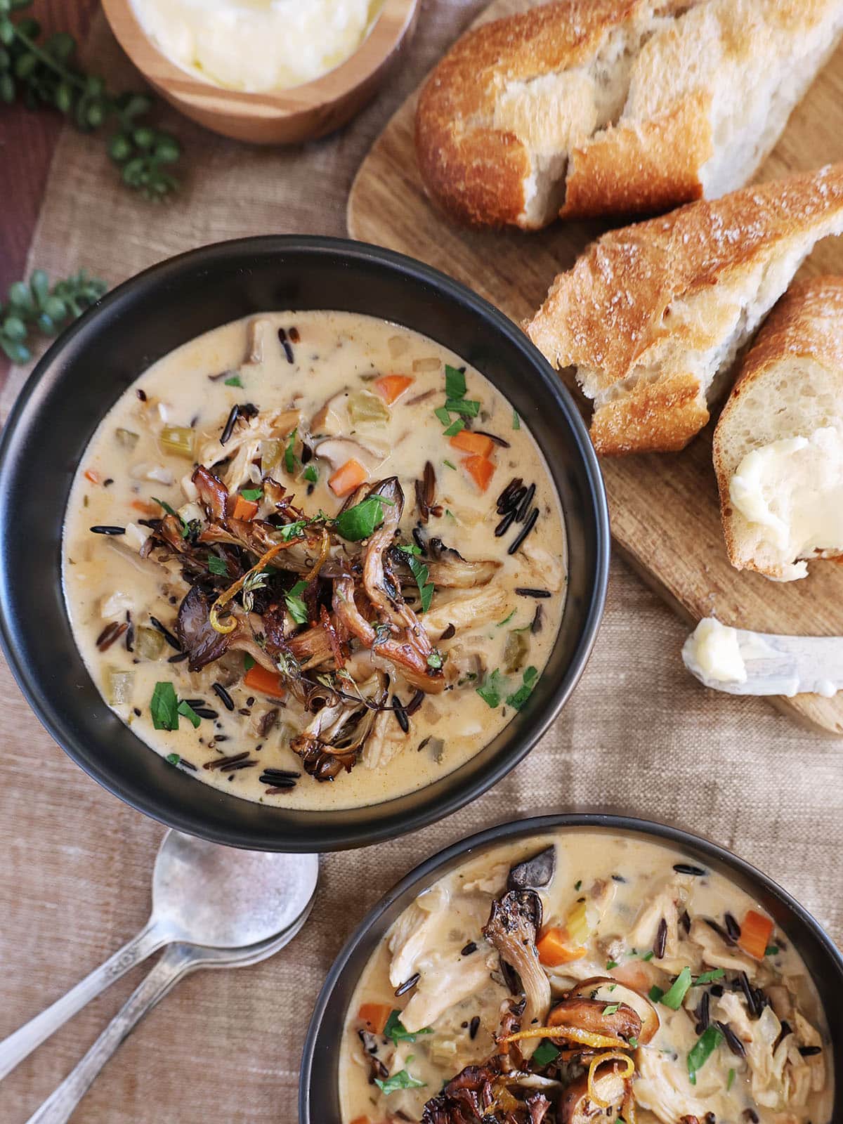 Two bowls of creamy chicken mushroom soup next to crusty bread.