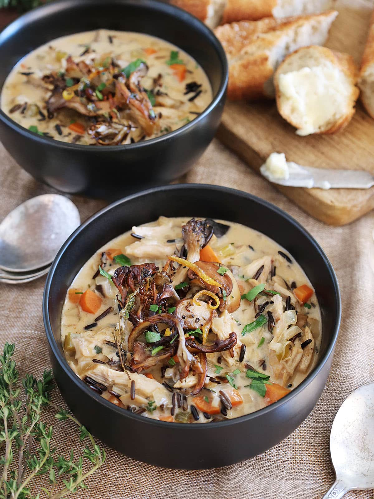 Two bowls of chicken mushroom soup next to crusty bread.
