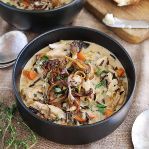 Side view of a black bowl of chicken mushroom soup topped with crisped mushrooms.