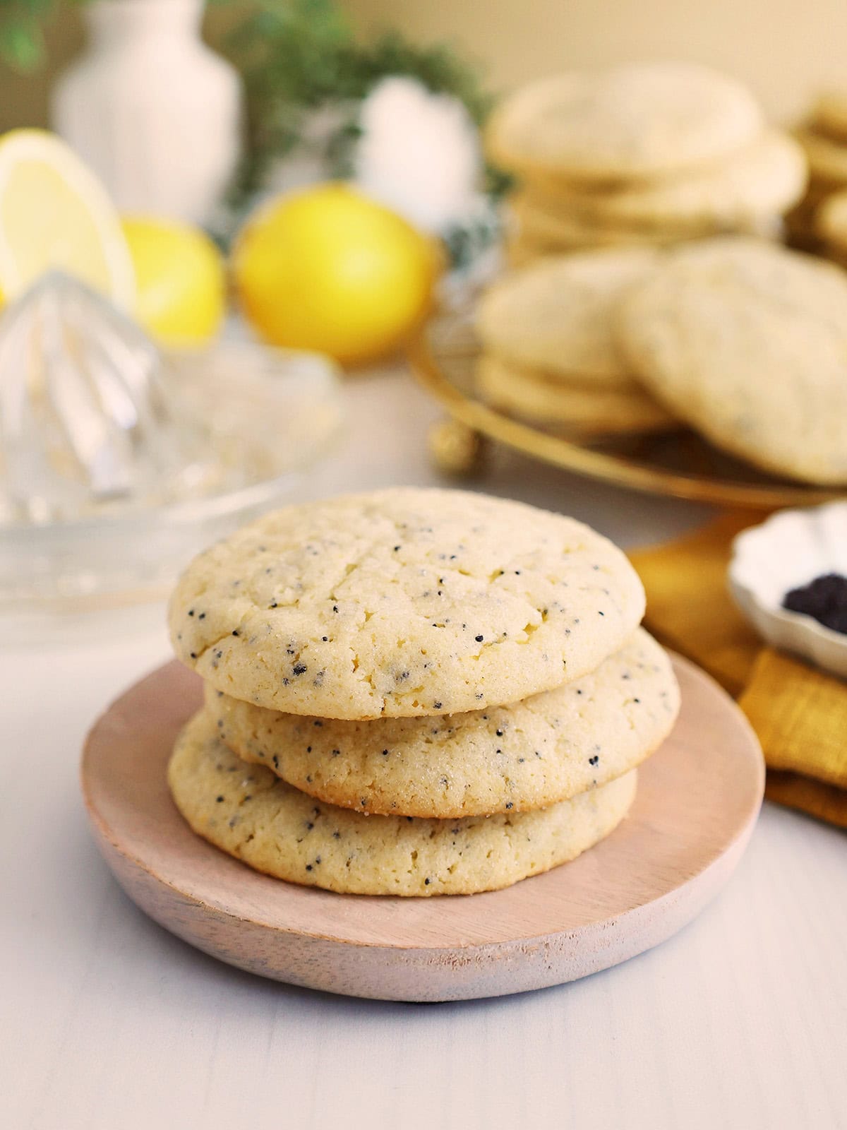 Three lemon poppyseed cookies stacked one on top of the other on a small wooden plate.