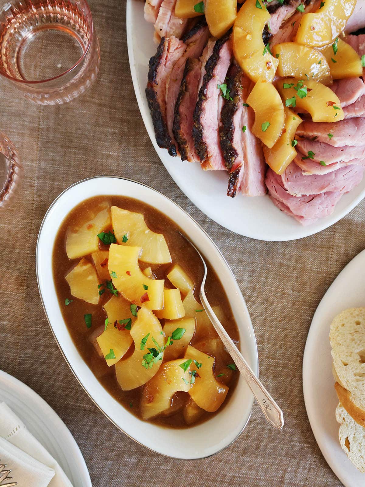 Top view of an oblong bowl filled with pineapple sauce next to a platter of slice ham topped with more sauce.
