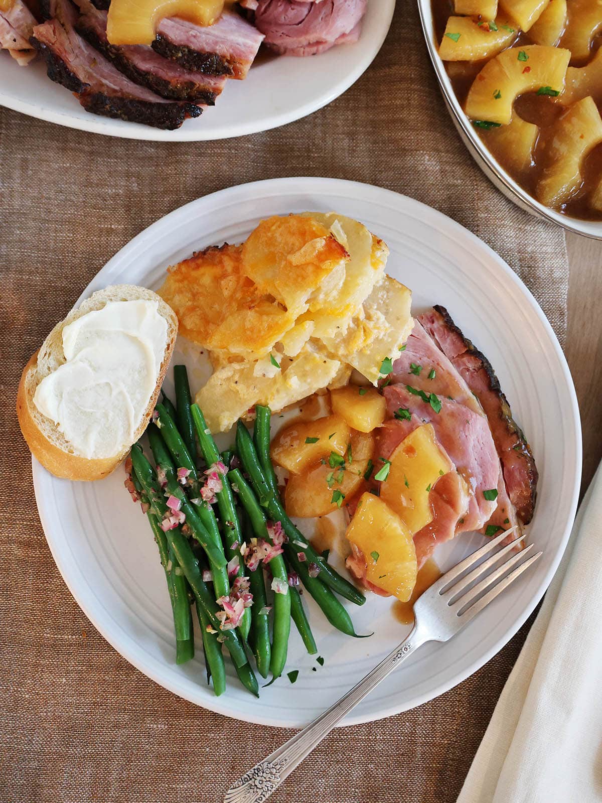 Top view of a plate filled with a holiday meal including sliced ham topped with pineapple sauce.