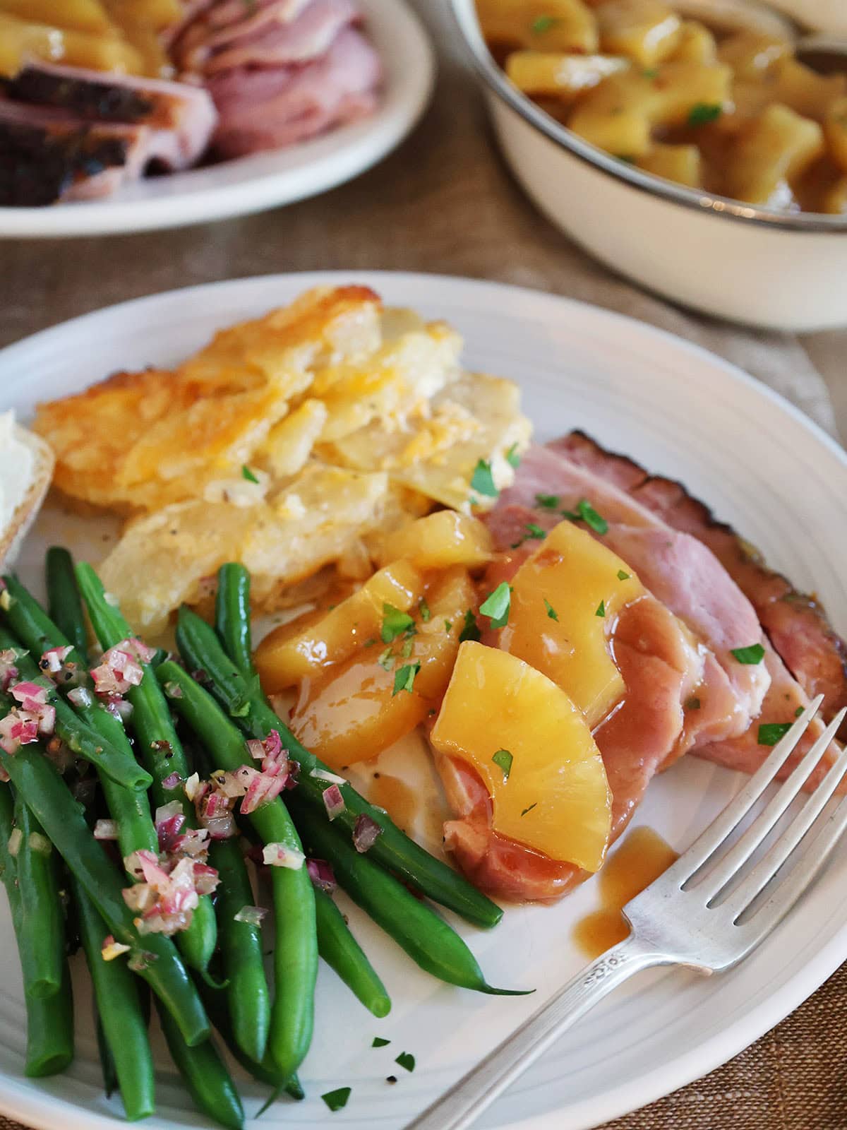 Close up of a holiday meal on a plate with ham topped with pineapple sauce.