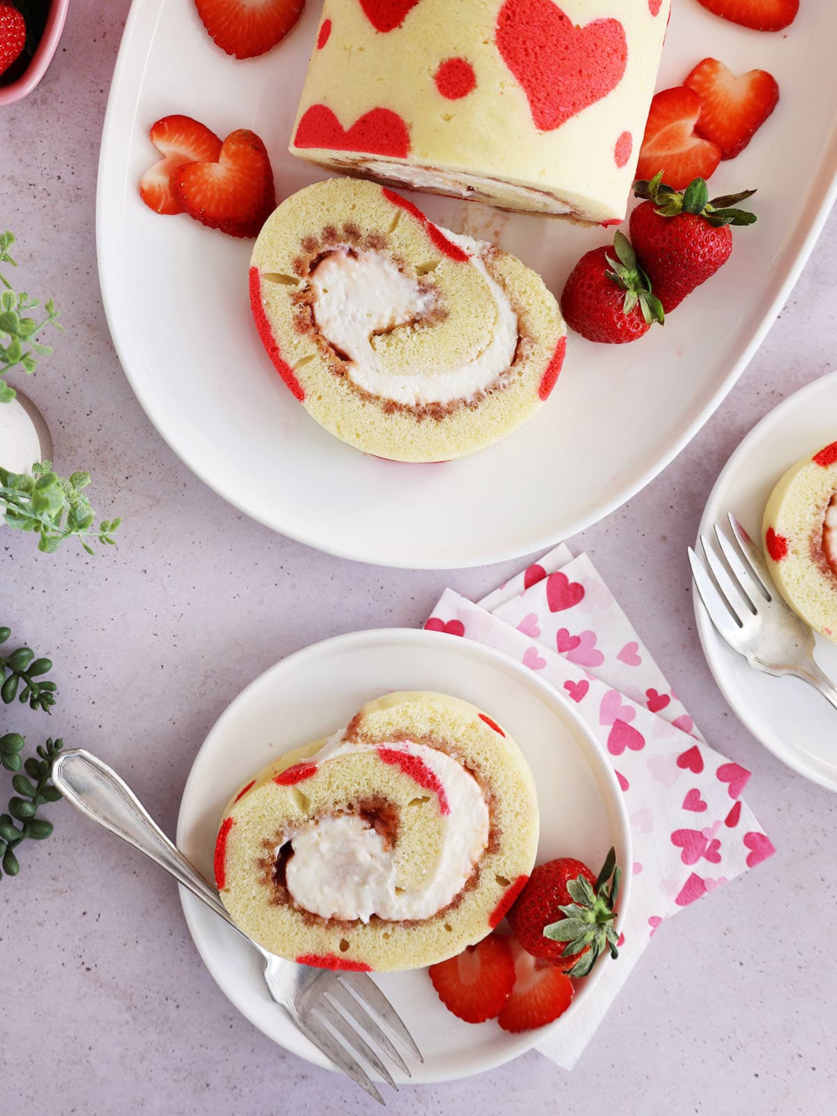 Top view of a slice of Valentine's Day strawberry cake roll on a small plate with the rest of the cake on a larger platter.