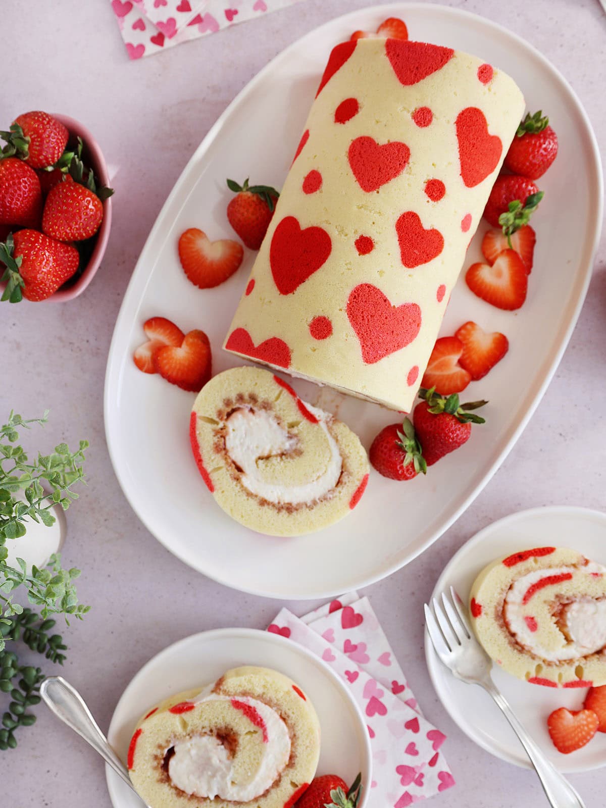 A decorated Valentine's Day strawberry cake roll on a white platter.