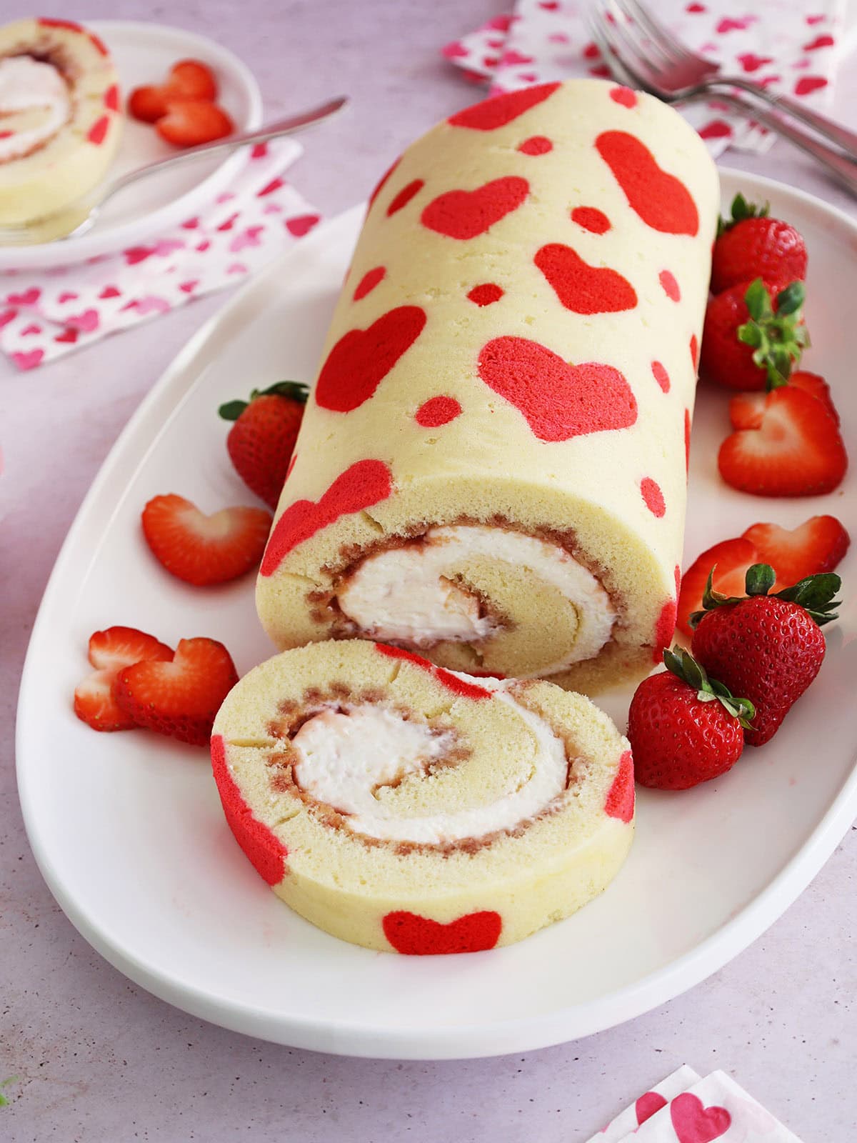 Valentine's Day strawberry cake roll with one slice cut off on a white platter.