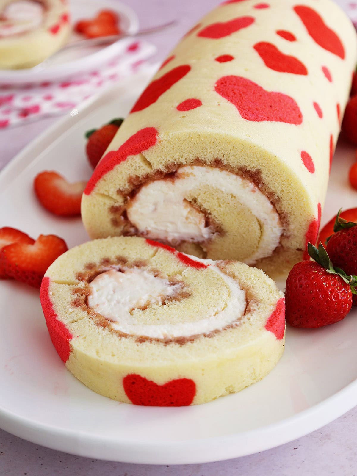 Close up of a Valentine's Day strawberry cake roll with a slice cut off on a white platter.