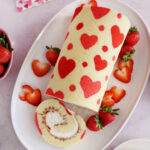 Close up of the top of a Valentine's Day strawberry cake roll with a slice removed on a white platter.