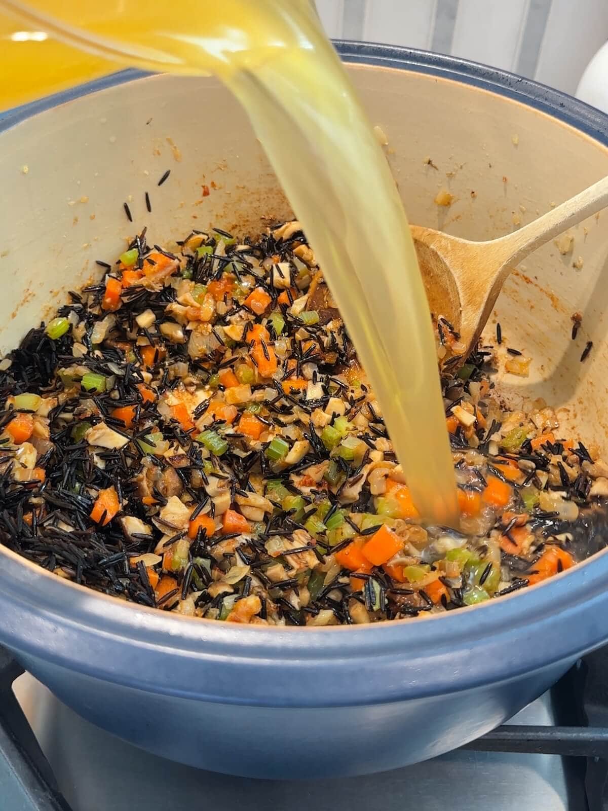 Adding broth to vegetables and rice in a pot