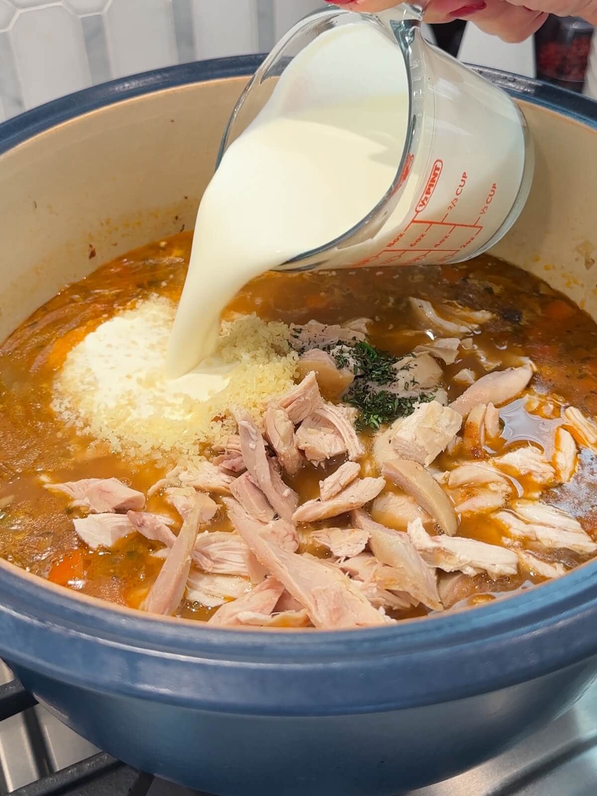 Adding cream and Parmesan to a pot of chicken wild rice soup.