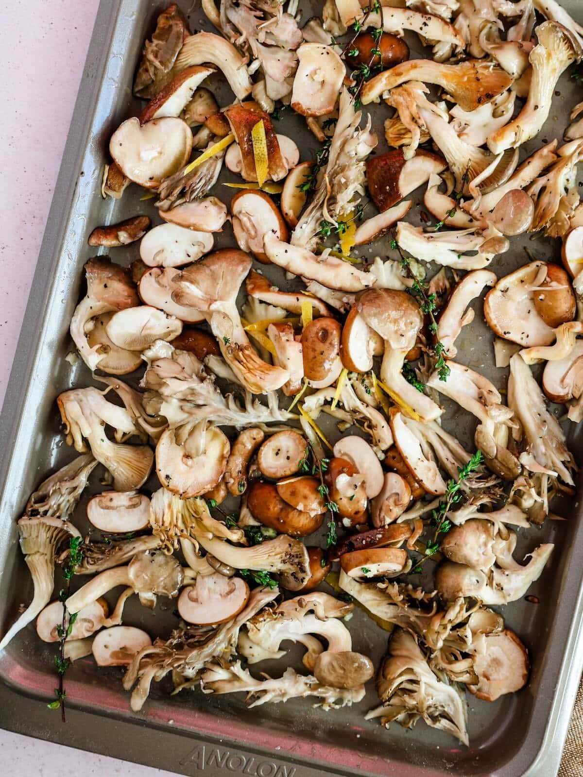 Raw mushrooms, lemon zest, thyme, and seasonings on a sheet pan ready to roast.