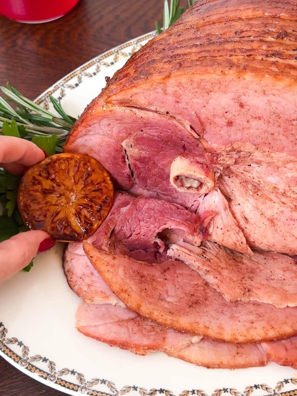 Finished ham on a platter with garnishes.