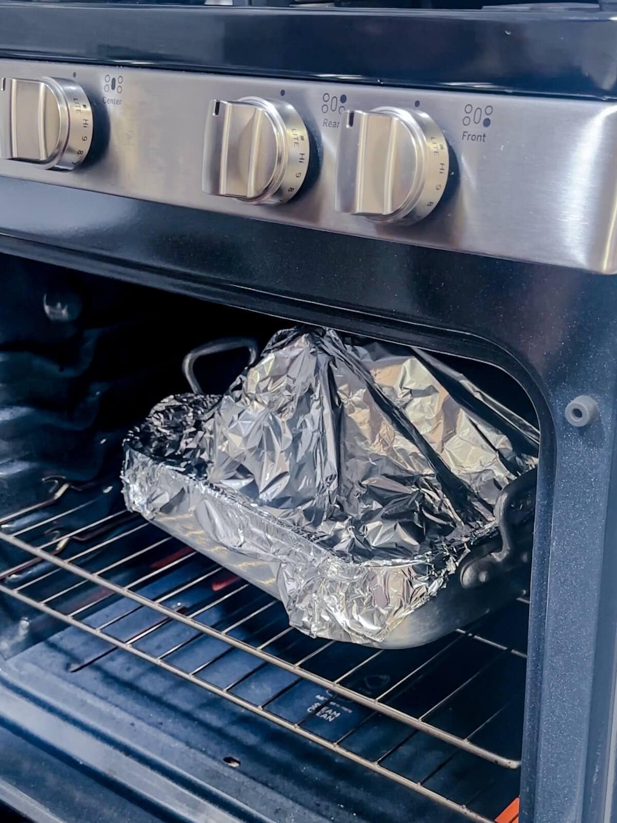Ham in a roasting pan with tinfoil tented over the top of it in an oven.