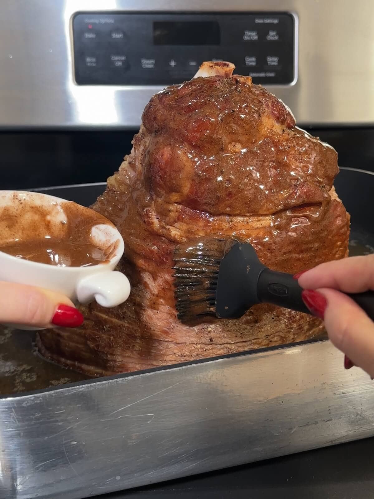 Hand brushing honey glaze over a a partially baked ham.