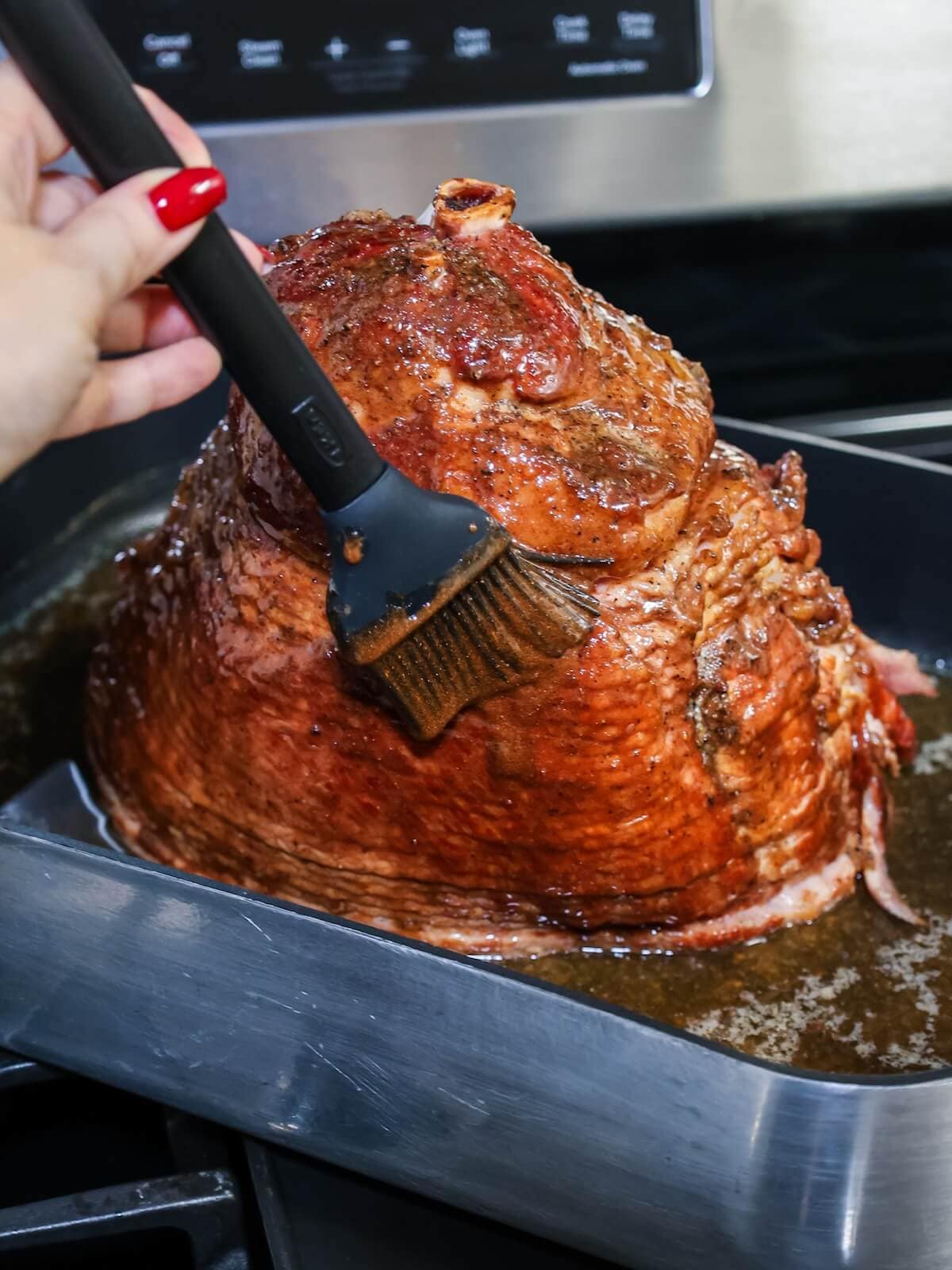Hand spreading honey glaze over the top of a ham.