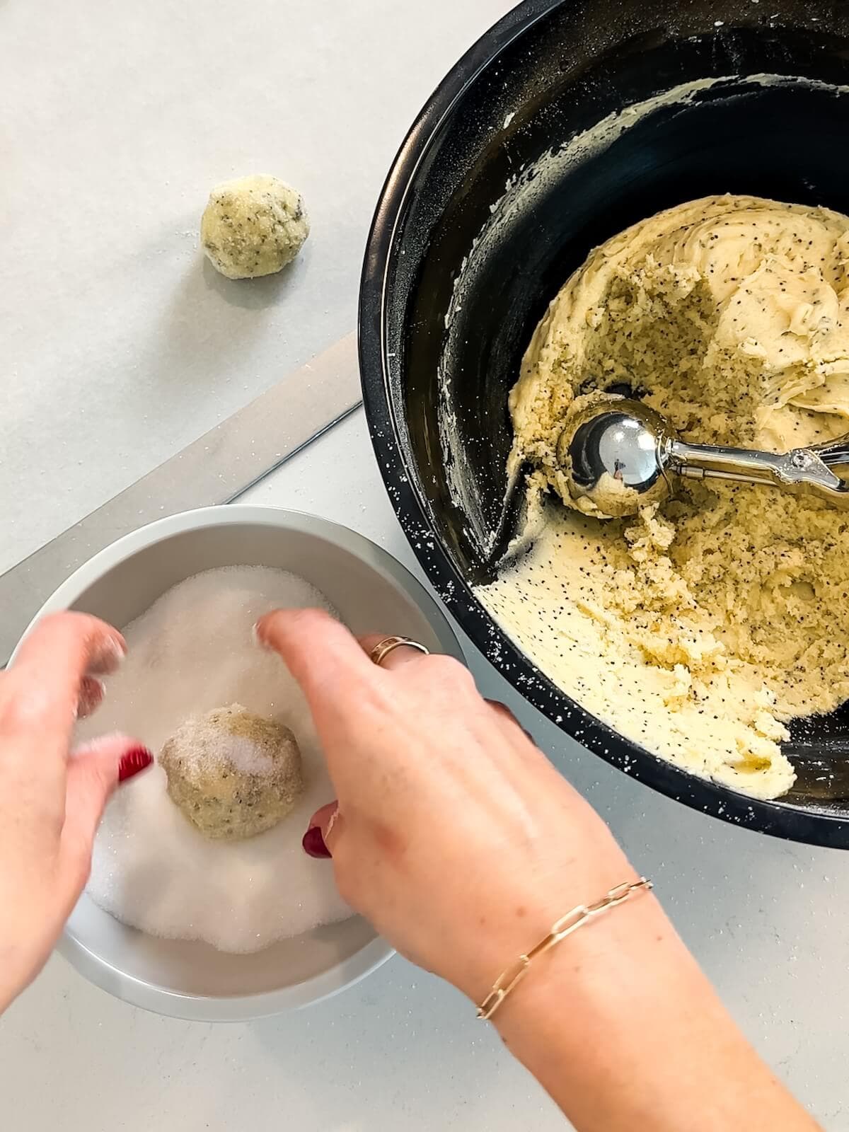 rolling balls of lemon poppyseed dough in sugar before baking.