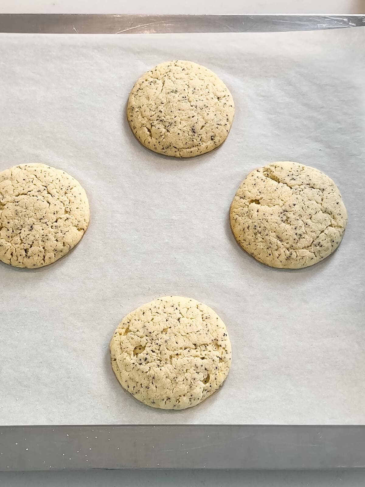 Baked lemon poppyseed cookies on a baking sheet showing baked edges and cracked tops.