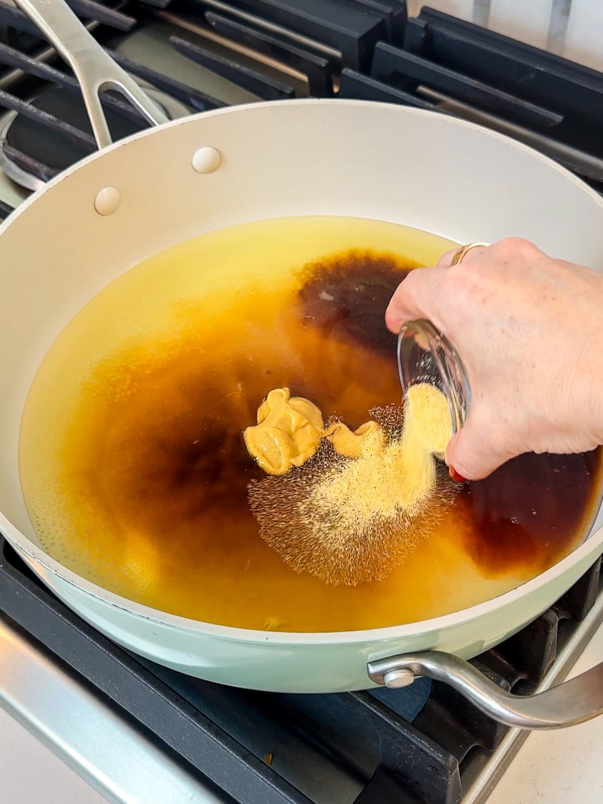 Adding pineapple juice and other ingredients to a pan to make pineapple sauce for ham.