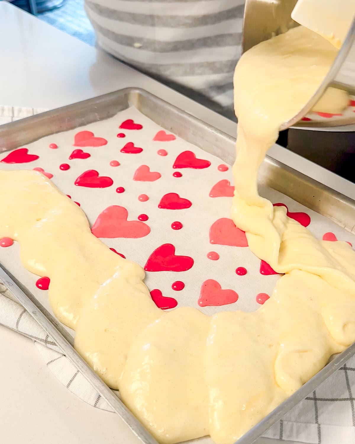 pouring cake batter over heart designs in jelly roll pan.