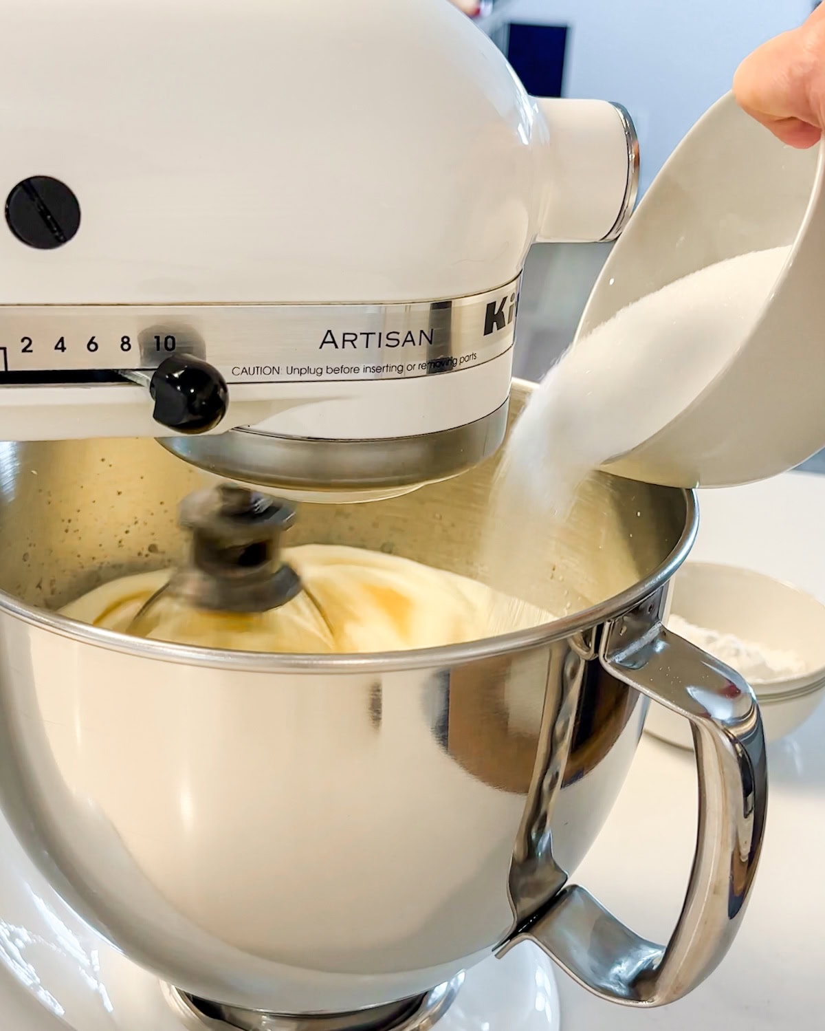 gradually adding sugar to cake batter as it whips in stand mixer.