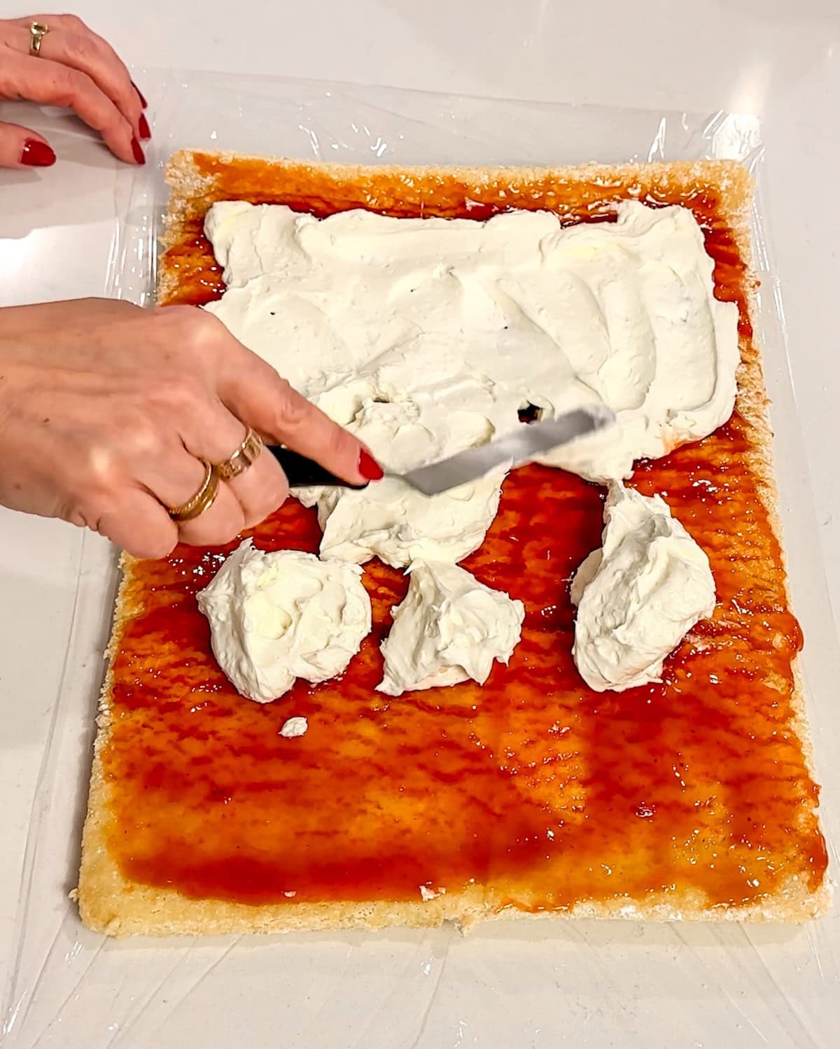 spreading jam then cream cheese filling on cake before rolling up.