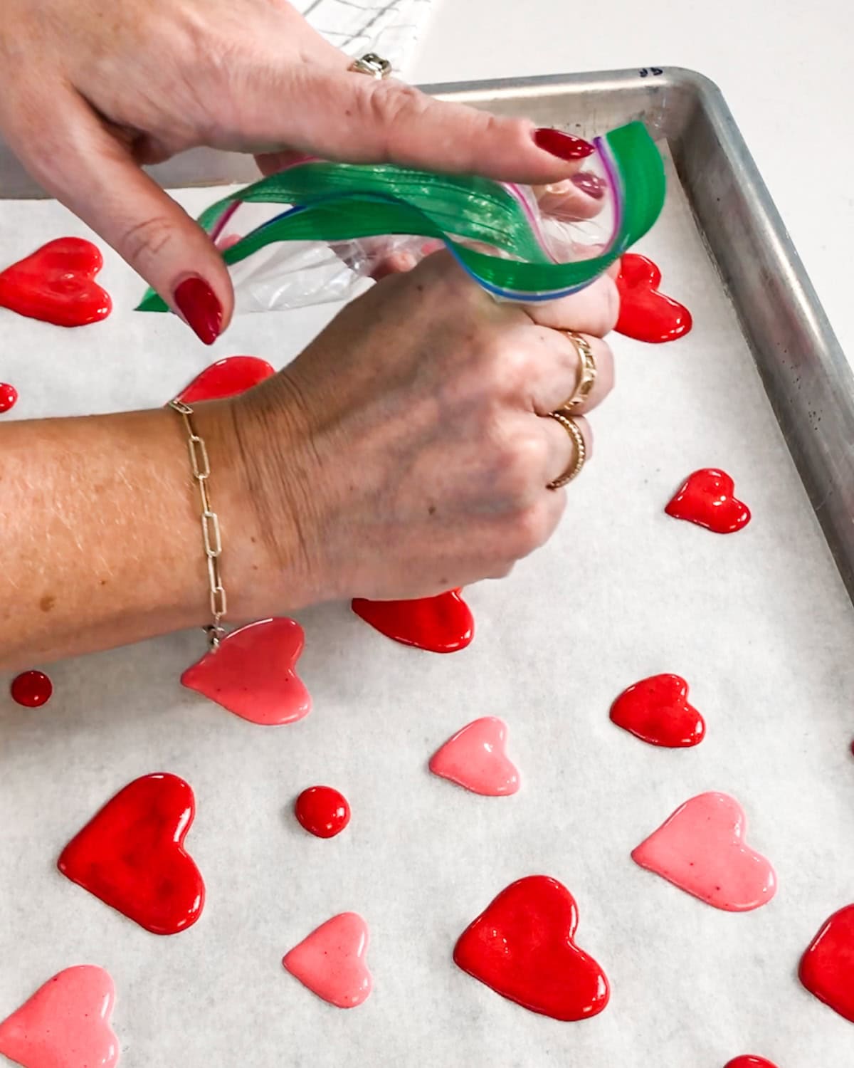 user piping colored batter into heart shapes on a parchment-lined jelly roll pan.