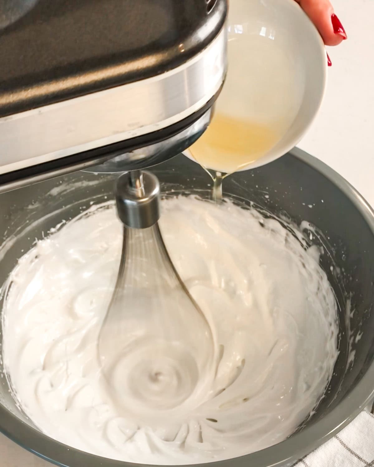 adding oil in slowly to a bowl of whipped egg whites and sugar.
