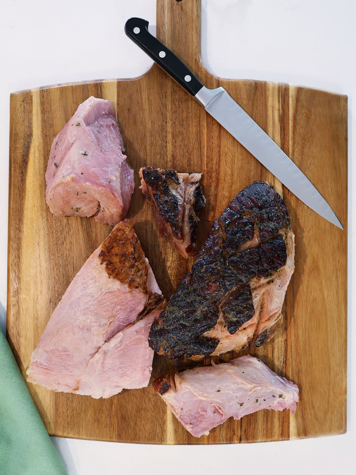 Large pieces of boneless ham on a cutting board by a knife.