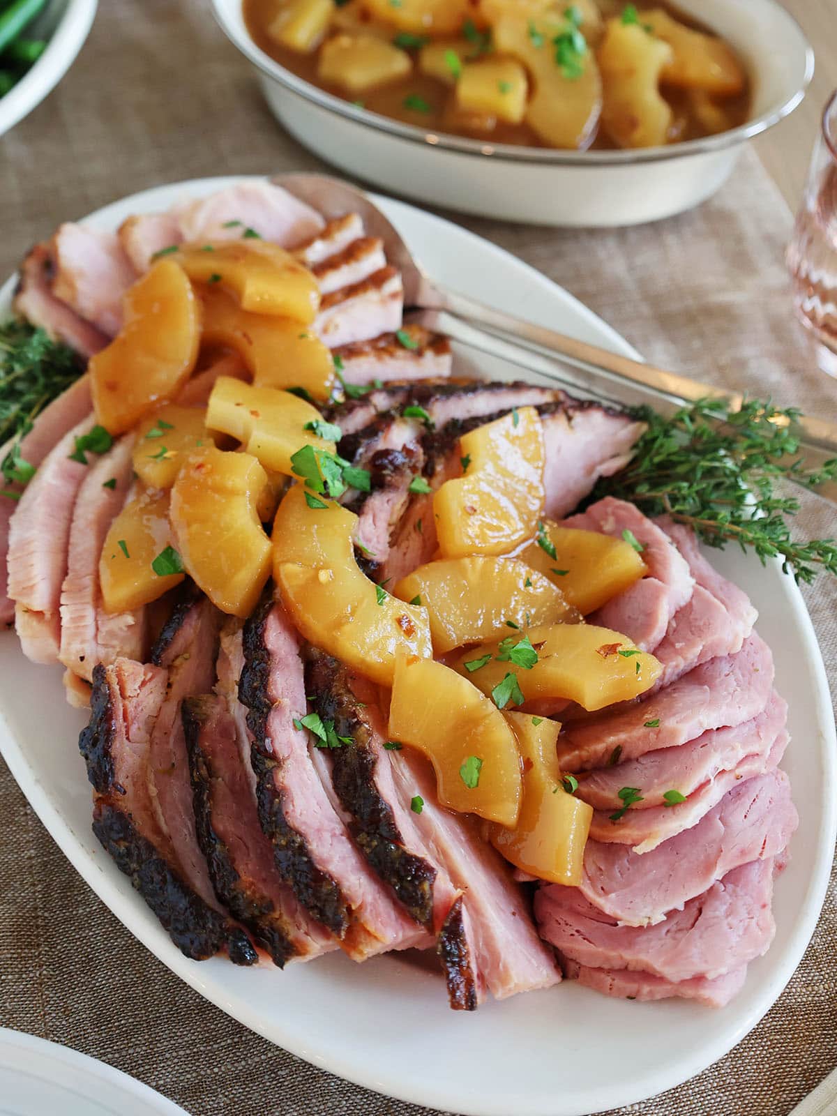 A honey roasted ham laid across a platter and topped with pineapples.