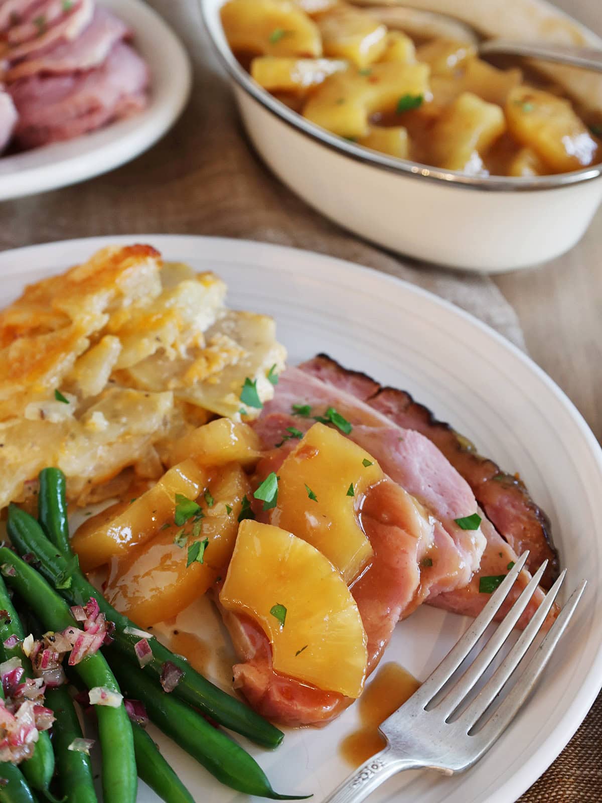Close up of a serving of pineapple roast ham on a dinner plate that is topped with pineapple.