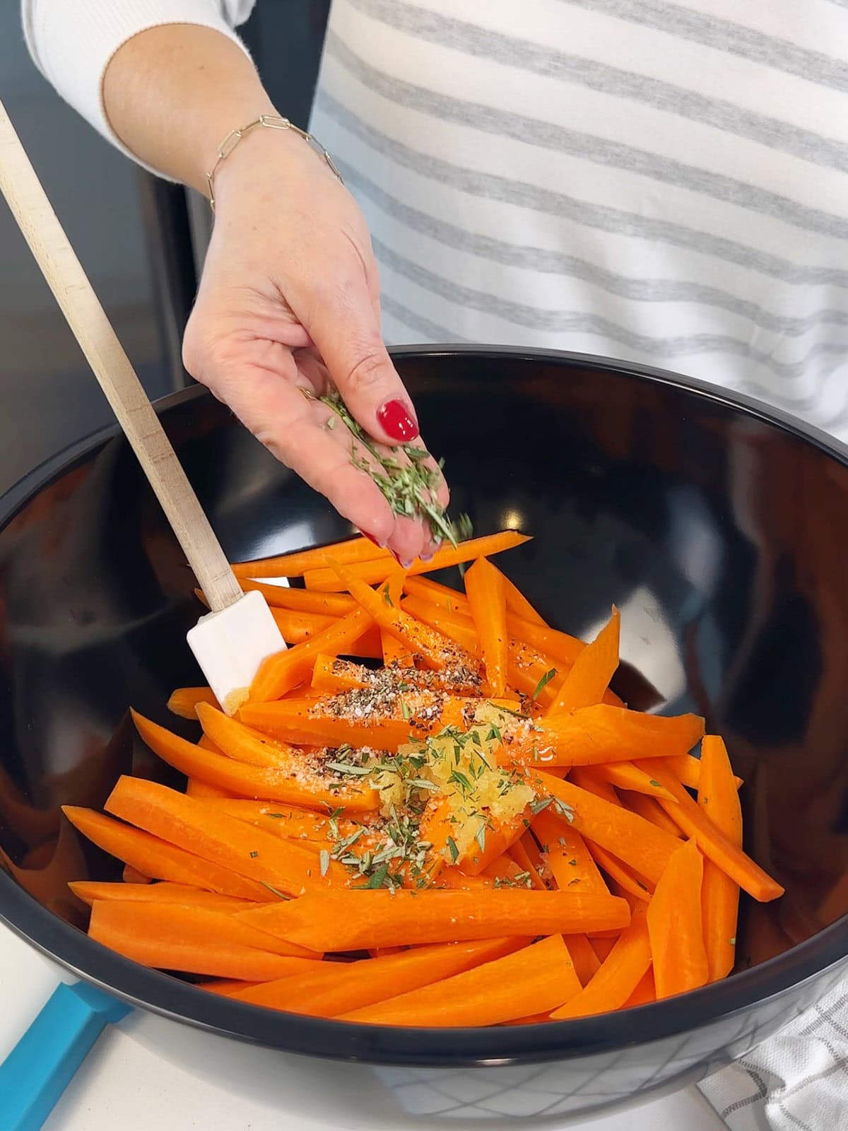Adding rosemary, garlic, salt and pepper to carrots for honey roasted carrots.