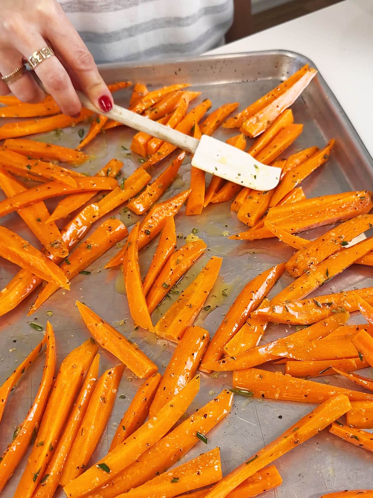 spreading carrots sticks on a sheet pan in an even layer for roasting.