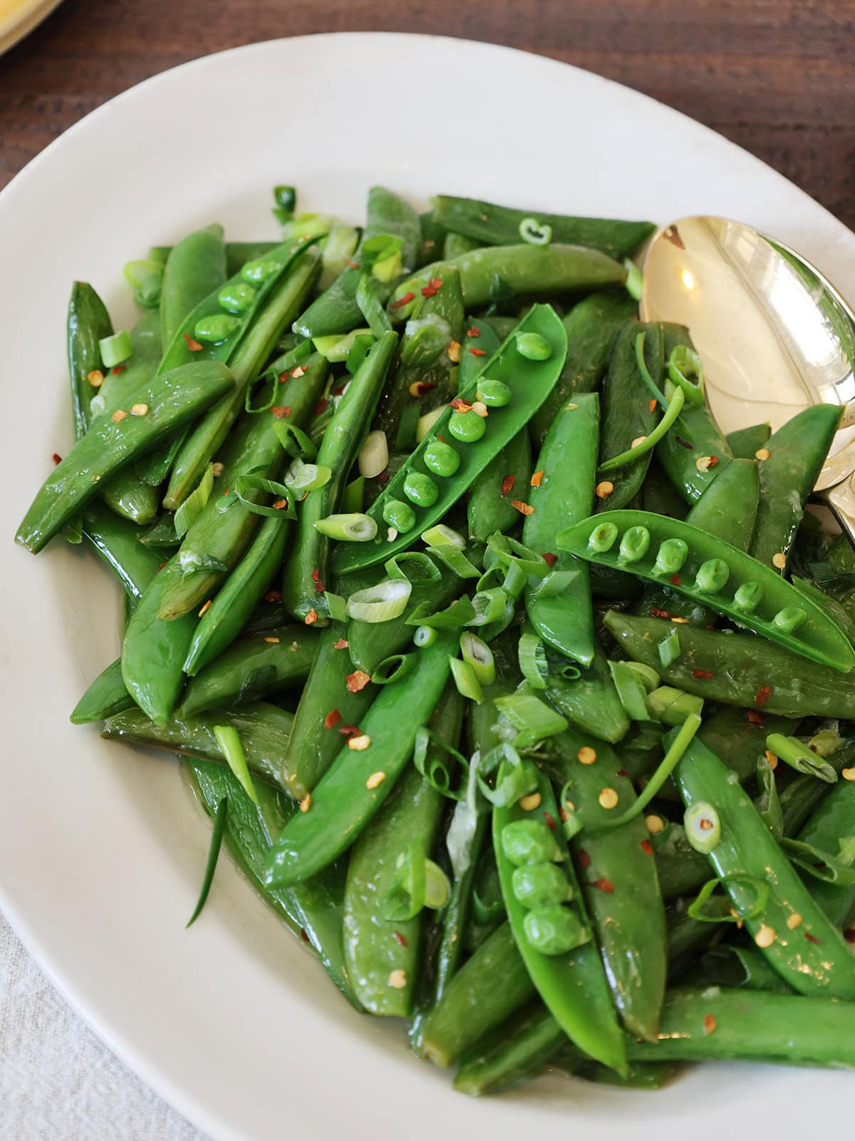 Overhead view of sauteed sugar snap peas sprinkled with scallions and pepper flakes.